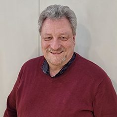 Bild vom Geschäftsführer Thomas Mayr-Kiessling mit grauen Haaren, lächelnd, in rotem Pullover vor hellem Hintergrund.